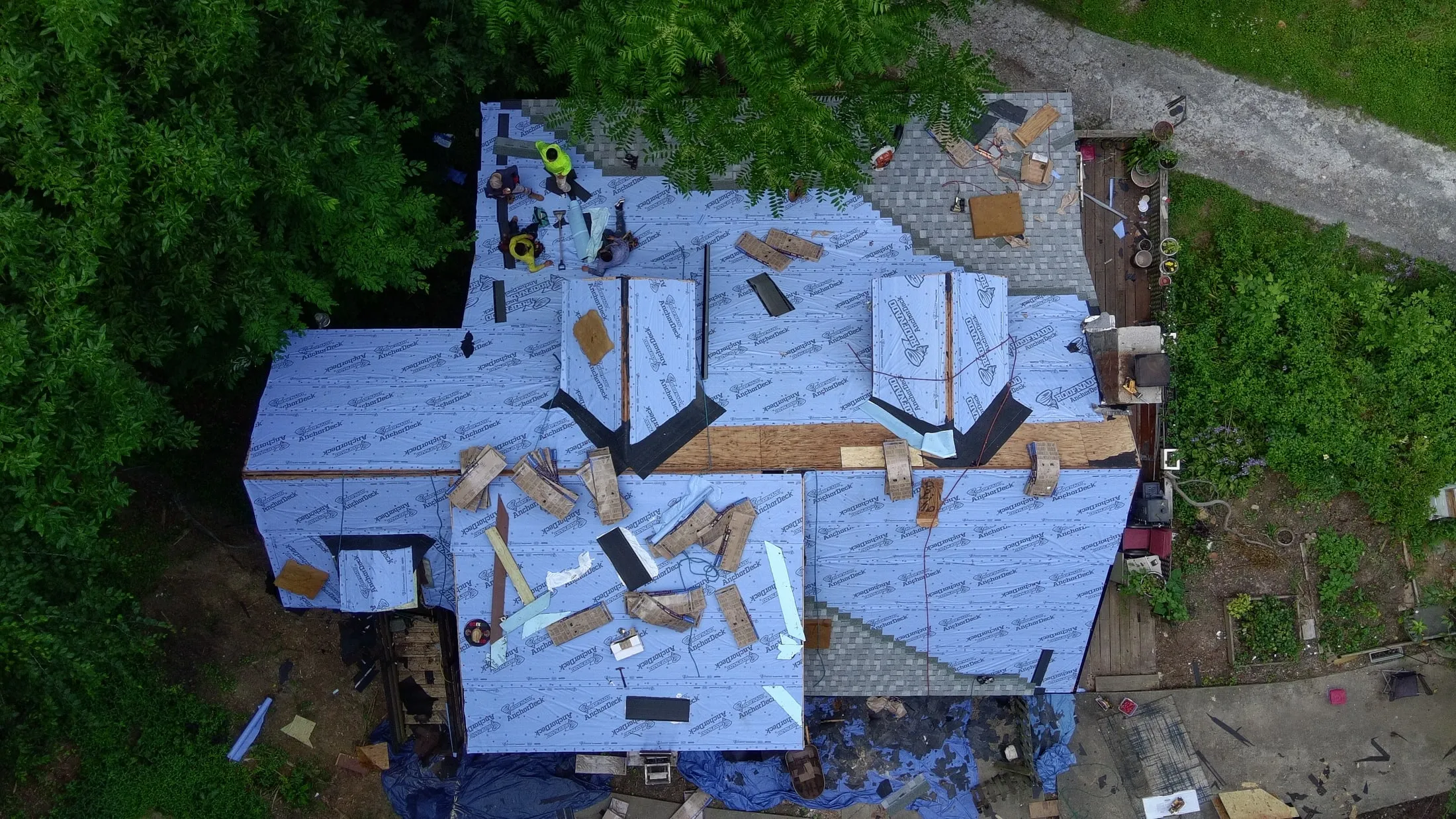 Iron Ridge crew installing new underlayment on a roof, with tarps laid over the ground below to catch debris
